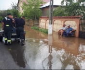 Fotografia zilei vine din Teleorman. Doi localnici stau pe banca in timp ce pompierii scot apa din comuna